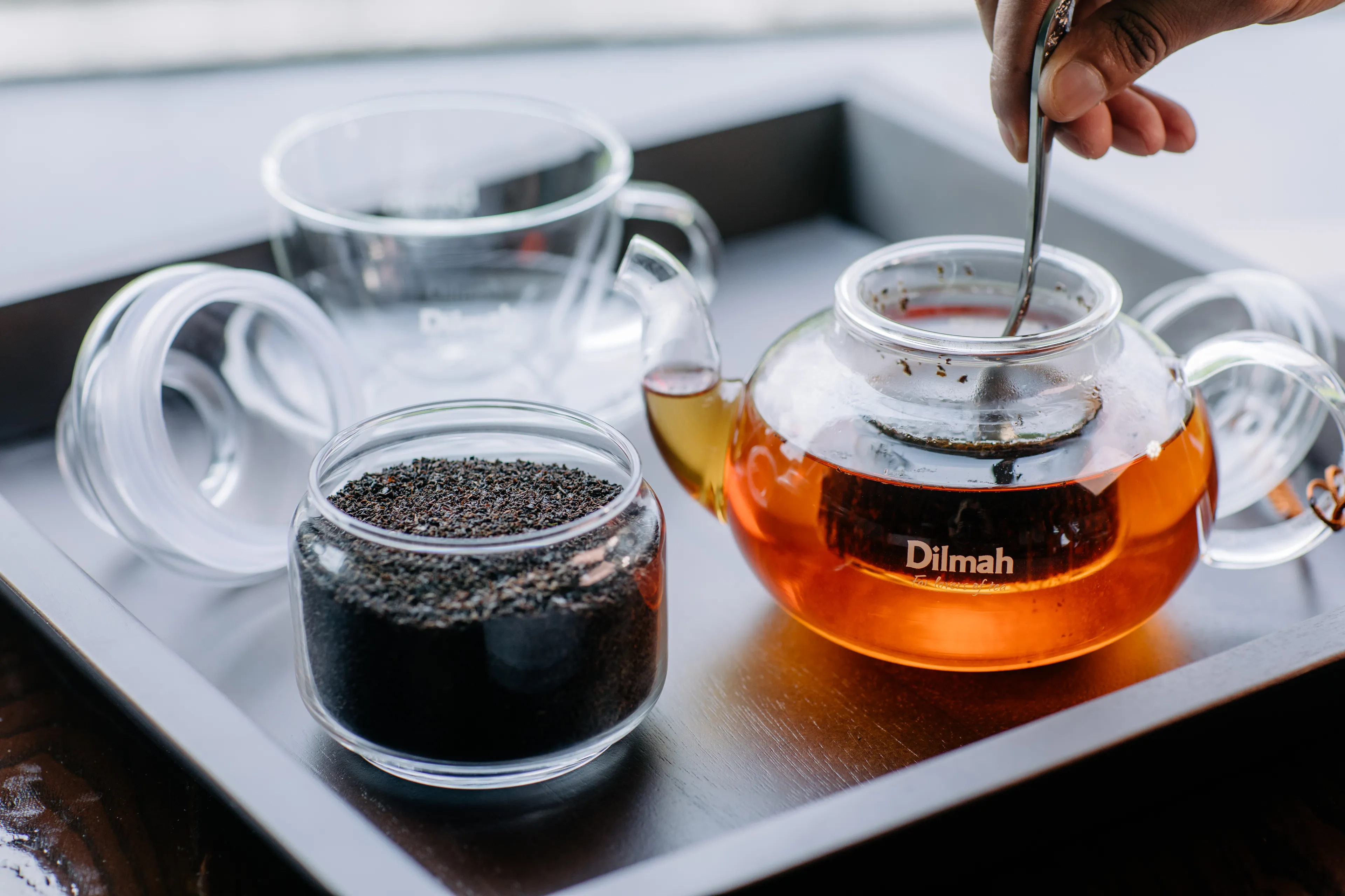 Loose leaf tea jar and a hand stirring the infused tea in a glass tea pot