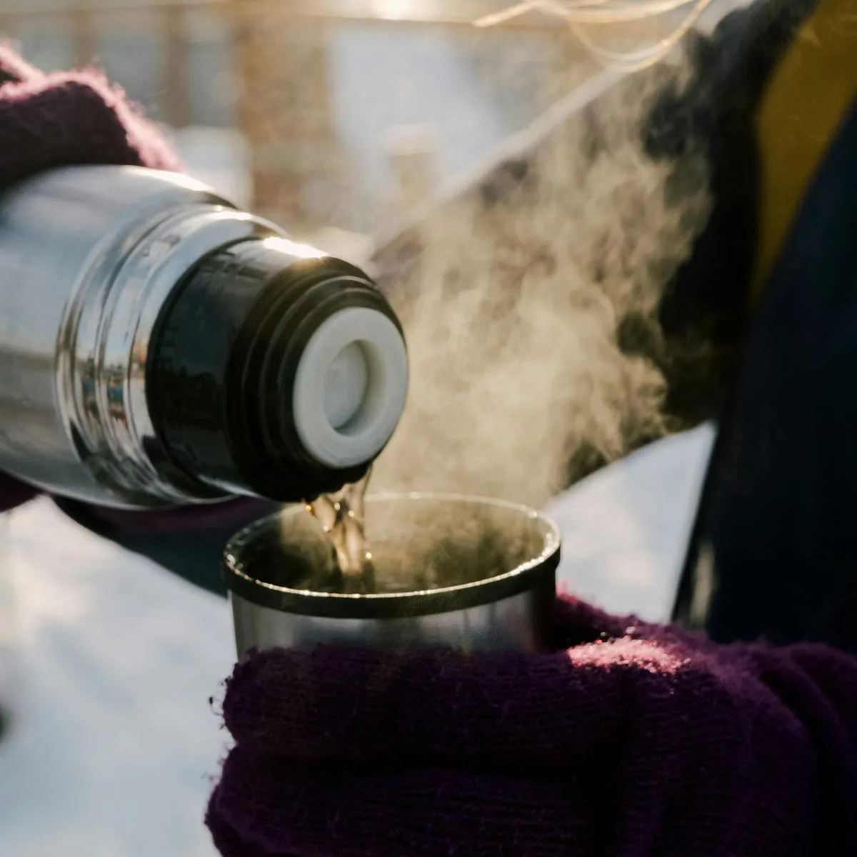 Person, die heißen Tee aus einer Thermoskanne in einer Tasse serviert, an einem kalten Tag